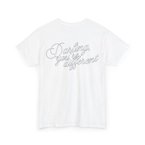 Può includere: Una t-shirt bianca a maniche corte con il testo "Darling, you're different" stampato in un sottile corsivo nero al centro del petto. La maglia presenta un girocollo, una vestibilità standard, maniche corte e un orlo dritto sul fondo.