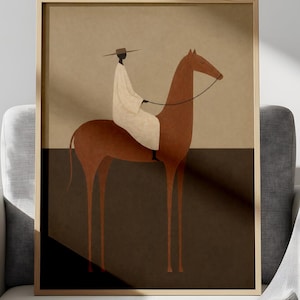 May include: Framed art print featuring an illustration of a person riding a horse. The rider is wearing a white garment and hat. The horse is brown, and the background is divided into tan and dark brown sections. The artwork is displayed in a gold frame.
