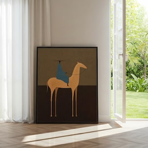 May include: Framed art print featuring a minimalist illustration of a rider on a camel. The artwork has a tan camel, a blue-clad rider, and a dark brown and olive green background. The print is displayed in a room with a window and white curtains.