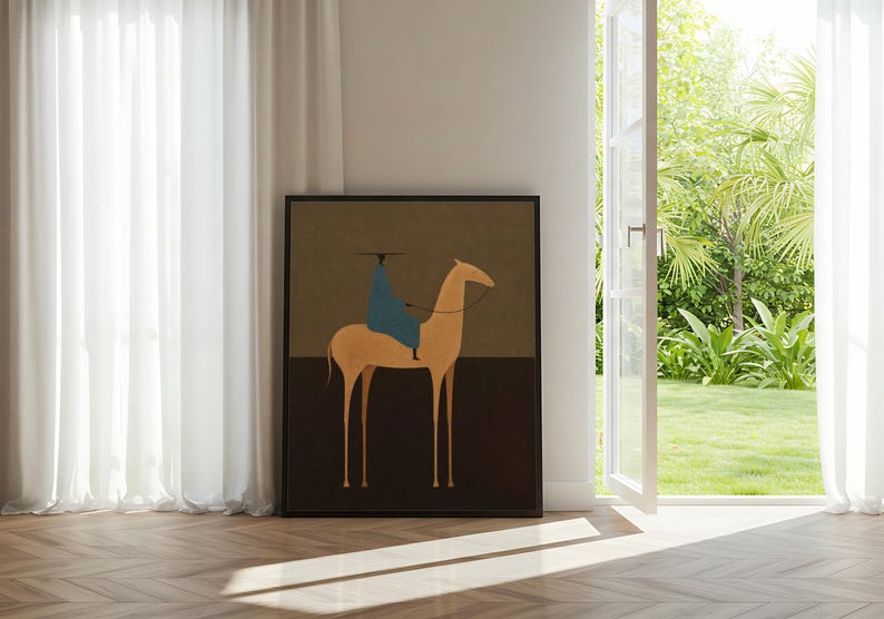 May include: Framed art print featuring a minimalist illustration of a rider on a camel. The artwork has a tan camel, a blue-clad rider, and a dark brown and olive green background. The print is displayed in a room with a window and white curtains.