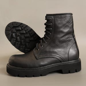 May include: A pair of black leather combat boots. They feature a lace-up design with metal eyelets and a chunky, lugged sole. The boots have a padded collar and a sturdy, durable construction. The boots are designed for both style and practicality.