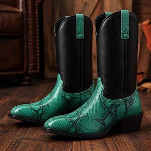 May include: A pair of mid-calf boots featuring a solid black upper shaft and a vibrant green snakeskin-textured lower foot. The boots include matching green pull tabs at the top, a pointed toe, and a stacked heel, showcasing a distinct two-tone design.