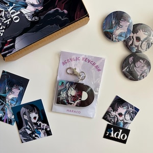 Könnte beinhalten: Eine Sammlung von Fanartikeln mit Anime-Charakterillustrationen, bestehend aus einem Karton, drei runden Ansteckbuttons, zwei quadratischen Aufklebern, einem rechteckigen Aufkleber mit dem Text Ado und einem Acryl-Schlüsselanhänger in Plastikfolie.