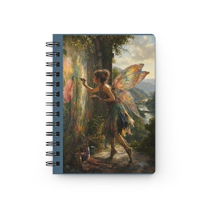 May include: Spiral-bound notebook featuring a vibrant illustration of a fairy artist painting a mural. The fairy has colorful wings and is dressed in a green and blue outfit. The background shows a landscape with a river and mountains.