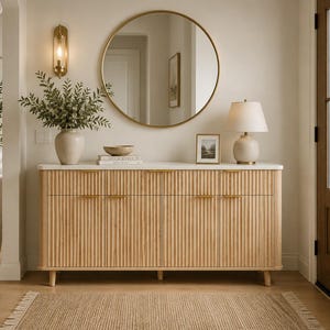 May include: A light wood sideboard with a white top and vertical fluted detailing on the cabinet doors. The piece features thin gold horizontal handles, stands on short tapered legs, and provides a flat surface for decorative items.