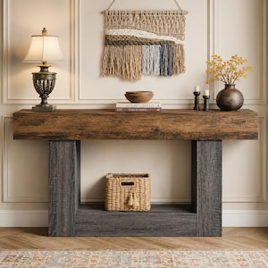 May include: A rectangular console table with a natural wood grain top and dark gray, textured vertical supports. The table features a lower shelf holding a woven wicker basket with tassels. A lamp, books, a bowl, and a vase sit on the surface.