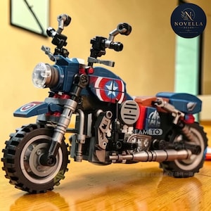 Puede incluir: Un modelo de motocicleta hecho con bloques de construcción en color azul oscuro, con emblemas circulares de estrellas en rojo y blanco en los laterales. El vehículo de juguete incluye un faro transparente, neumáticos negros, tubos de escape plateados.