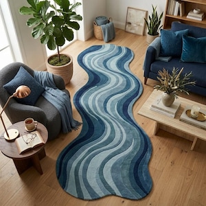 May include: An elongated, organic-shaped area rug featuring a wavy, multi-tonal pattern in shades of blue, ranging from light sky blue to deep navy. The rug has a textured, tufted surface with curved lines that mimic the flow of water across the floor.