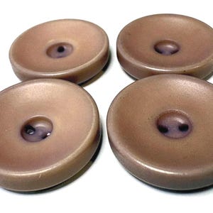 Peut inclure: Quatre boutons ronds et concaves dans une teinte mauve-brun atténuée. Chaque bouton présente une finition lisse et mate avec un centre légèrement évidé contenant deux petits trous pour la fixation. Les boutons sont disposés en grille.