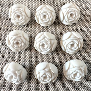 May include: A set of nine off-white buttons, each shaped like a carved rose with layered petals. The buttons are arranged in a three-by-three grid, featuring a smooth, matte finish and a rounded, dimensional floral design on the front surface.