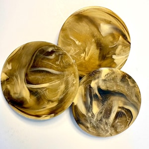 Può includere: Tre sottobicchieri circolari caratterizzati da un motivo marmorizzato vorticoso nelle tonalità del marrone scuro, marrone chiaro e crema. La superficie di ogni sottobicchiere ha una finitura liscia e lucida con linee fluide e complesse.
