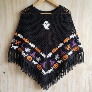May include: A black crocheted poncho featuring a white ghost motif at the neckline and a repeating pattern of orange pumpkins, purple witch hats, white bats, white cats, and white spiderwebs along the bottom edge, finished with black fringe.