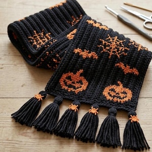 May include: A black knitted scarf featuring orange patterns of pumpkins, bats, and spiderwebs. The scarf has a ribbed texture and is finished with six black yarn tassels, each accented with a small orange crocheted spider at the top.