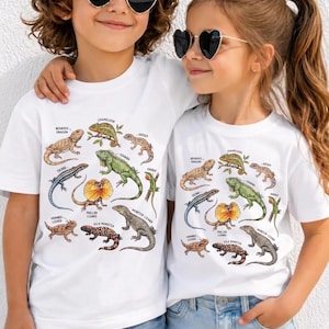 Könnte beinhalten: Zwei weiße kurzärmelige T-Shirts mit einem farbenfrohen Grafikdruck verschiedener Echsen, darunter eine Bartagame, ein Chamäleon, ein Gecko, ein Skink, ein Leguan, ein Anolis, eine Kragenechse, eine Krötenechse, eine Gila-Krustenechse und ein Waran.