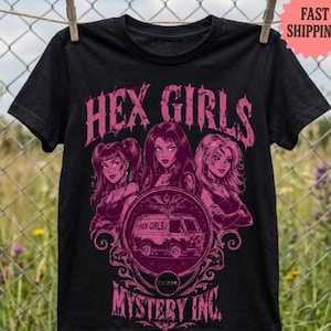 May include: A black short-sleeve t-shirt featuring a pink graphic print of the Hex Girls with the text "HEX GIRLS" above and "MYSTERY INC." below. The central design includes a circular frame containing a van illustration with the text "HEX GIRLS".