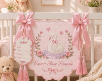 May include: A pink scalloped fabric wall hanging featuring an embroidered white swan, floral wreath, and butterflies. The text reads Emma Rose Bennett. A smaller attached tag includes lines for Date, Time, Weight, and Length. Pink satin bows and tassels.