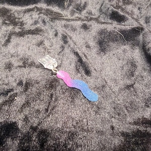 May include: A small, handmade earring with a clear, rectangular top and a wavy, worm-like charm. The charm is a gradient of pink and blue, attached by a silver-colored ring.