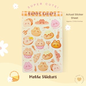 May include: A sheet of matte stickers featuring cute cartoon illustrations of bakery items, including bread, pastries, and cupcakes. The sticker sheet is titled "Bunny Bakery" and says "Super Cute!" at the top. The sheet measures approximately 3.7 by 5.4 inches.