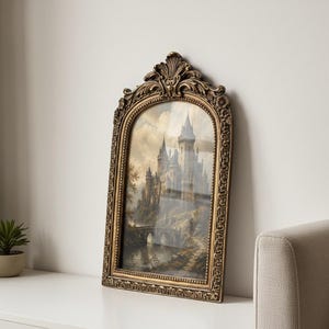 May include: An arched wall art piece featuring a detailed painting of a stone castle with towers and a bridge over water. The artwork is encased in an ornate, antique gold-coloured frame with intricate floral and scrollwork carvings at the top.