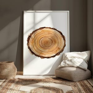 Op de afbeelding: Aquarel schilderij van een boomdoorsnede in een witte lijst. Het kunstwerk toont concentrische ringen in bruin- en beigetinten, met een donkerbruine boombastrand. De ingelijste kunst staat tegen een muur in een kamer met een vloerkleed en een mand.