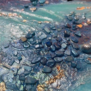 Könnte beinhalten: Abstraktes Kunstwerk mit strukturierter Oberfläche, das eine Mischung aus Blau-, Grün- und Goldtönen aufweist. Dunkelblaue Steine sind über die Oberfläche verstreut, mit dem Wort "Flut" in weißem Text.