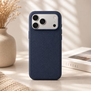 May include: A navy blue smartphone case with a textured, cross-hatched finish. The case features a raised, rectangular camera cutout with a silver-toned metallic border, housing three circular camera lenses and a small circular flash component.