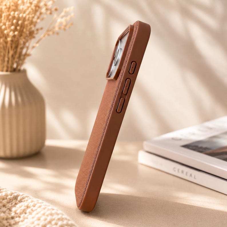 May include: A solid brown smartphone case with a textured fabric finish on the back and sides. The case features a raised camera cutout, integrated side buttons for volume control, and a slim profile designed to fit a mobile device securely.