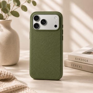 May include: A sage green smartphone case with a textured, cross-hatched surface. The case features a rectangular camera cutout at the top, revealing three circular camera lenses and a flash module arranged in a triangular configuration.