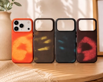 May include: Four colorful phone cases are displayed on a wooden surface. The cases are orange, brown, dark blue, and maroon. Each case has a rectangular camera cutout and a unique color pattern. The orange case has a star-like design.