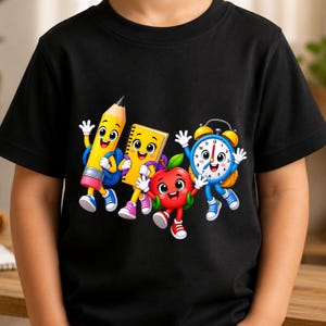 Pode incluir: Uma t-shirt preta de manga curta com um gráfico colorido de quatro materiais escolares antropomórficos: um lápis amarelo, um caderno de espiral amarelo, uma maçã vermelha e um despertador azul, todos com rostos sorridentes.