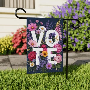Peut inclure: Un drapeau de jardin rectangulaire sur fond bleu foncé orné d'un arrangement floral coloré composé de fleurs roses, violettes, jaunes et blanches. Le mot VOTE est imprimé en grandes lettres capitales blanches au centre du motif.