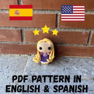 Puede incluir: Una muñeca de ganchillo con cabello rubio y un vestido morado. La muñeca está frente a una pared de ladrillos, con las banderas estadounidense y española y tres estrellas doradas encima. El texto "PDF PATTERN IN ENGLISH & SPANISH" está debajo.