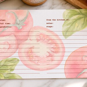 May include: Recipe card with watercolor illustrations of tomatoes and basil. The card has lines for recipe details, including recipe, total time, and ingredients. The text "from the kitchen of: notes: steps:" is also visible.
