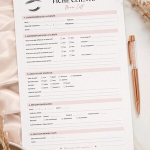 Peut inclure: Une fiche client pour un Brow Lift, avec des sections pour les informations du client, l'historique médical et l'analyse des sourcils. Un stylo rose doré avec des accents en cristal est posé sur le côté droit.