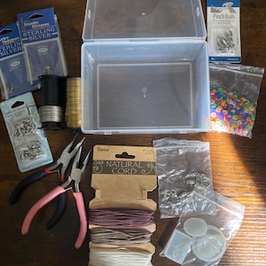 May include: A jewelry making kit containing a clear plastic storage box, two spools of wire, two pairs of pliers with pink and black handles, assorted sterling silver findings, pinch bails, colorful flat beads, natural cord, and silicone molds.