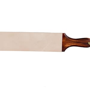 May include: A leather sharpening strop featuring a rectangular light beige leather surface attached to a dark brown polished wooden handle. A short, light-coloured cord loop is threaded through a hole at the end of the wooden handle for hanging.