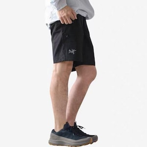 May include: Black shorts with a small logo on the left leg. The shorts have pockets and are paired with dark blue athletic shoes. The person is wearing a light-colored long-sleeve shirt.
