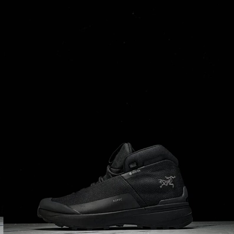 May include: Black high-top hiking boot. The boot has a mesh upper and a thick sole. The word "KOPIC" is printed on the side. A bird logo is visible on the side of the boot. The boot is designed for outdoor activities.