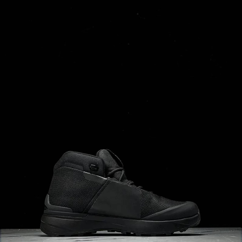 May include: A black high-top boot with a mesh and smooth texture. The boot has a thick sole and a padded collar. The design is sleek and modern, suitable for various outdoor activities. The boot is approximately 18 cm tall.