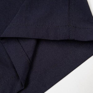May include: Close-up of navy blue fabric, showing the folded hem and stitched seam. The fabric appears to be a medium-weight material, with a slight sheen. The image is well-lit, highlighting the texture and color of the textile.