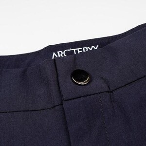 May include: Close-up of navy blue pants with a button closure. The brand name "ARC'TERYX" is visible in white lettering on the waistband. The pants appear to be made of a smooth, durable fabric.