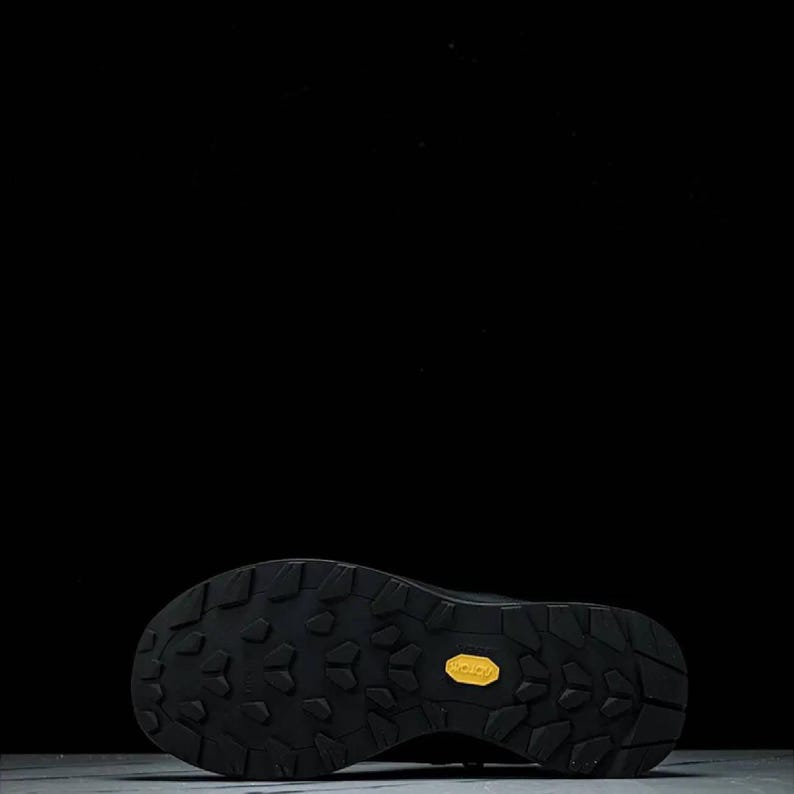 May include: Black hiking boot sole with a textured pattern and a yellow Vibram logo. The sole is designed for grip and durability, suitable for outdoor activities and rugged terrain.