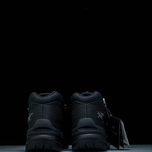 May include: Two black hiking boots with a textured upper and thick soles against a black backdrop. The boots have a high-top design and a small logo on the side. A tag is attached to one of the boots.