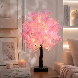 Puede incluir: Una lámpara decorativa en forma de árbol con un tronco texturizado de color marrón oscuro y una densa copa de pequeñas flores de color rosa claro con forma de cerezo. Las ramas están iluminadas por luces LED integradas de color blanco cálido.