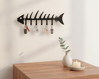 The product is a decorative key holder designed to resemble a fish skeleton Made from durable metal it features a sleek black finish that ad