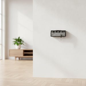May include: A black wall-mounted key holder designed to resemble a miniature guitar amplifier. The unit features a silver speaker grille, four control knobs along the top edge, and a Fender logo on the left side, with a single metal key inserted.