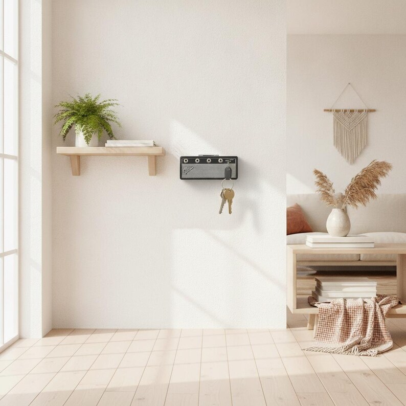 May include: A wall-mounted key holder designed to resemble a miniature black and silver guitar amplifier. The rectangular unit features a front grille, control knobs, and a jack input where a key ring with several metal keys is currently hanging.