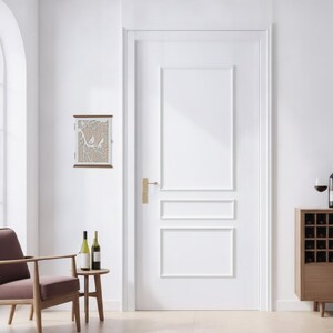 Peut inclure: Une armoire à clés murale rectangulaire dotée d'un cadre blanc et d'un panneau avant décoratif avec un motif découpé au laser représentant deux oiseaux perchés sur une branche d'arbre sur un fond beige clair, située à gauche d'une porte intérieure.