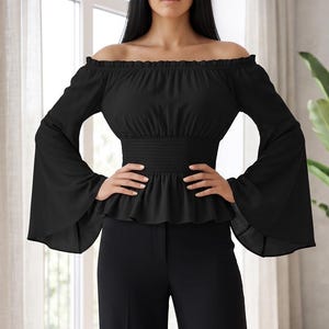 Puede incluir: Una blusa negra de hombros descubiertos con mangas largas acampanadas y cintura fruncida, combinada con pantalones negros a juego de pierna ancha. La blusa tiene un escote fruncido y un dobladillo con volante, y el pantalón es de corte recto.