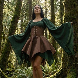 Può includere: Un abito verde bosco con maniche lunghe e ampie a campana e scollo quadrato. Il capo presenta un corpetto marrone in stile corsetto con chiusura frontale a lacci e una gonna svasata a strati che cade sopra il ginocchio in tinta unita.